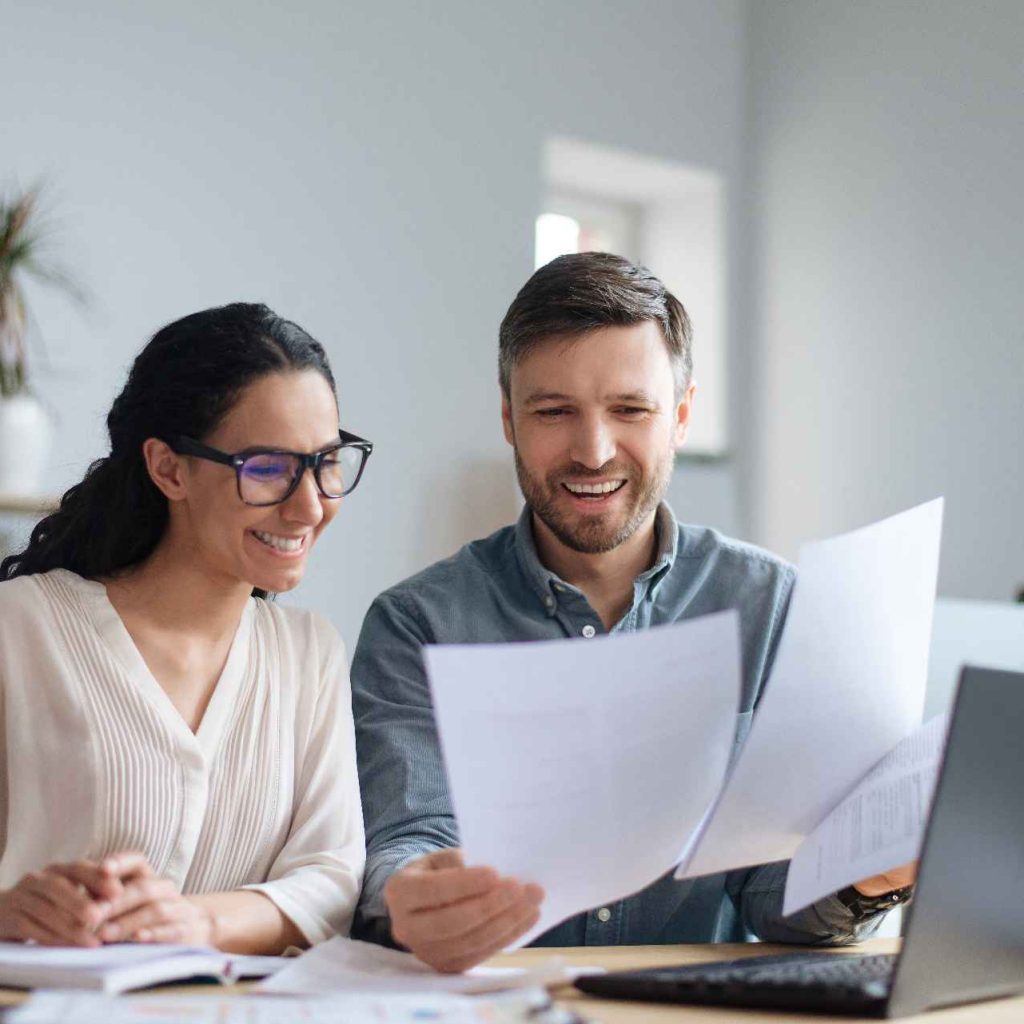 cheerful-male-female-company-workers-looking-through-documents-collaborating-using-laptop (1)